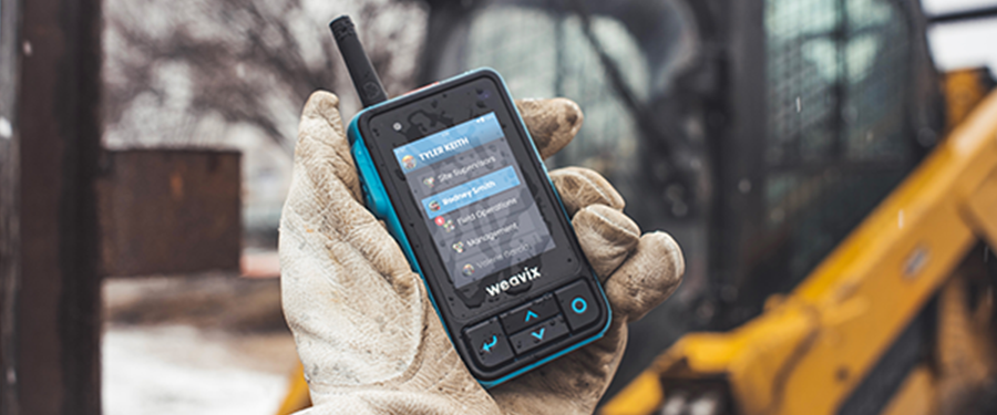 Close-up of a worker in the rain holding a Walt Smart Radio with water droplets on the screen, showing the many different channels available for audio, image, and video messages